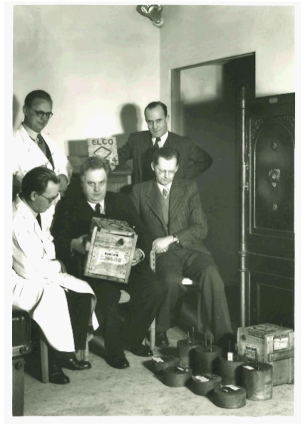 Figure 2: The Swedish medical physicist Rolf Siwert (middle) at the radiological clinic Röntgenheim in Stockholm around 1930. Siwert is seen with a box labeled "Radium"; and has taken to the ground are lead canisters of various sizes used to store the radium in small glass tubes. Source: Fijalken, Department of Radiophysics.
